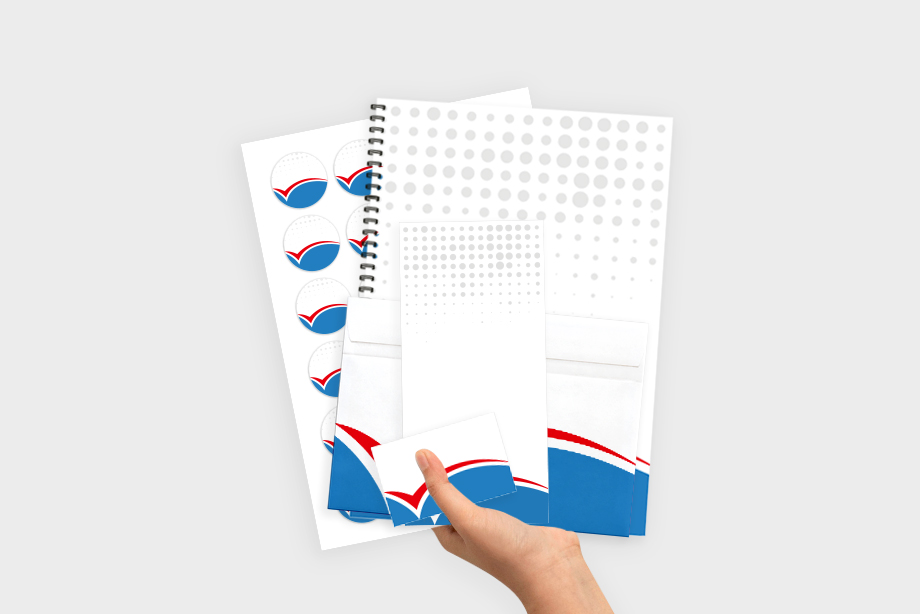 Hand hält eine Auswahl an individuell bedruckten Druckprodukten wie Aufkleber, Spiralblock, Umschlag, Notizblock und Visitenkarte – komplettes Drucksortiment von flyerwire