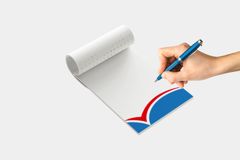 Hand schreibt mit Kugelschreiber auf individuell bedruckten Notizblock mit modernem Design in Blau, Rot und Weiß, freigestellt vor weißem Hintergrund – Notizblöcke drucken lassen